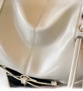Detailed close-up of glossy beige leather material with fine stitching and metal eyelets