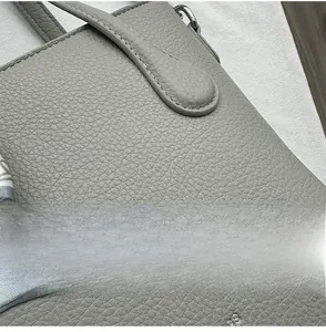 Nahaufnahme der grauen Lederhandtasche mit weißen Nähten und dekorativem Seidenschal-Detail