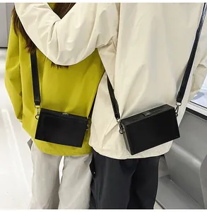 Fashionable black rectangular box crossbody bag with metal buckle shown on two models