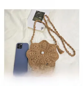 Detailed view of a brown woven floral crossbody bag with a large pearl and tassel accent