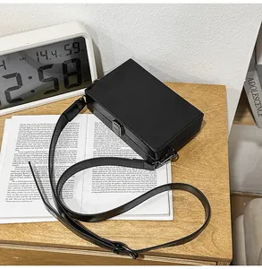 Detail shot of a black glossy box bag with silver metal clasp on a wooden desk with books