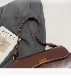 Dettaglio della borsa baguette in pelle marrone scuro con fibbia dorata su blazer grigio