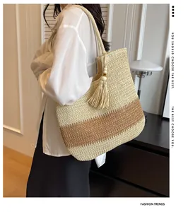 Detail view of woven straw tote bag in beige and brown with tassel on a female model