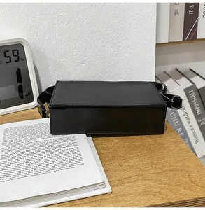 Detail of a minimalist black PU leather box bag on an open book and wooden table