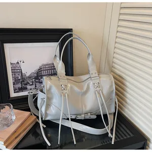 Detail of light grey glossy tote bag with lace-up decor and metallic studs on table