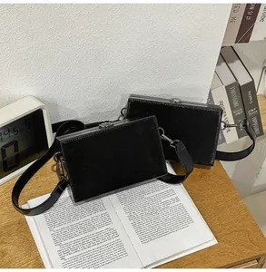Detail of black glossy PU leather box bag with silver metal clasp on a wooden table
