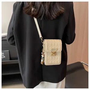 Detail of off-white quilted phone bag featuring golden twist lock and a cute bear charm