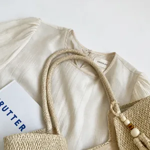 Detail of woven straw shoulder bag with tassels and beige short-sleeve top on white background