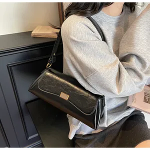 Dettaglio di una borsa baguette nera lucida con fibbia dorata su uno sfondo minimalista