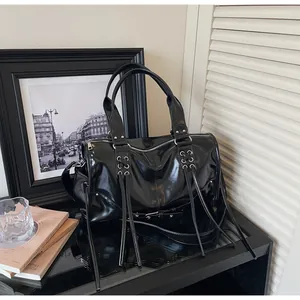 Detail of black glossy tote bag featuring long fringes and silver metal eyelets