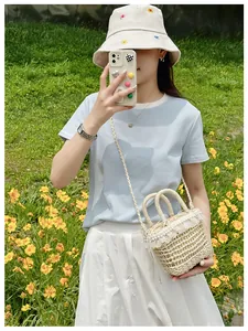Detail of straw crossbody bag with white lace, pearls, and drawstring closure in garden