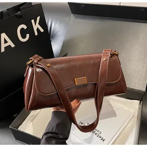 Dettaglio di una borsa a spalla in pelle marrone con fibbia dorata e confezione regalo