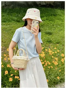 Detailed view of straw bucket bag with white lace trim and pearl accents on grass