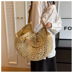 Detalle de bolso tote redondo grande de paja con correas de cuero marrón en modelo