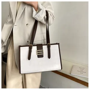 Detail of white crocodile pattern tote bag with brown leather trim and gold metal buckle