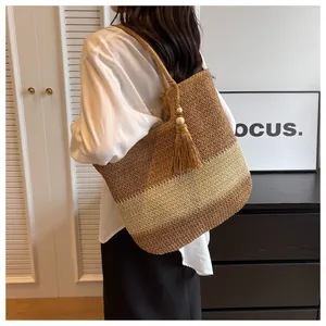 Detail of woven straw tote bag with brown stripes and decorative tassel pendant