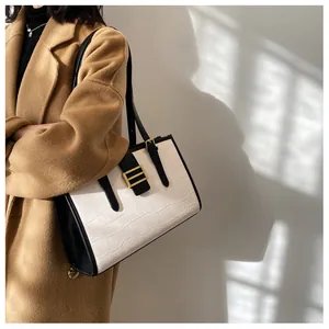 Side view of a large white faux crocodile tote bag with black strap and gold buckle