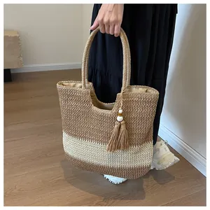 Detail of hand-woven straw tote bag with brown stripes and a decorative tassel accent