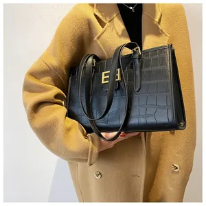 Detail of black crocodile pattern tote bag with gold buckle on camel coat model