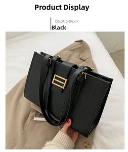 Detail view of a black tote bag with crocodile pattern and golden buckle on a beige suit
