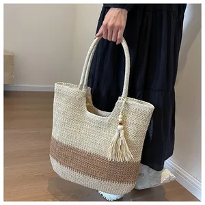 Detail of hand-woven straw tote bag featuring contrast stitching and wooden bead tassels