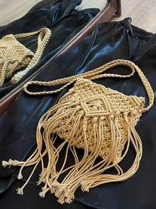 Beigefarbene Bohème-Macramé-Tasche mit Quasten auf schwarzem Seidenhintergrund