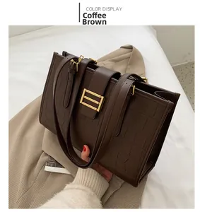 Detail of dark brown tote bag with crocodile texture and gold metal buckle on fabric