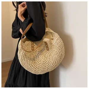 Detalle de bolso tote redondo de paja con correa de cuero marrón usado por una modelo