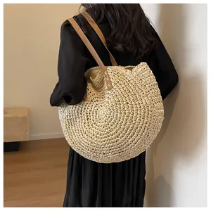 Detalle de un bolso tote redondo de paja con correas de cuero marrón y costuras en blanco