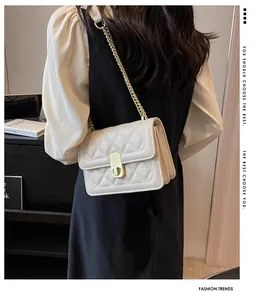 Détail d'un sac bandoulière matelassé beige avec chaîne dorée et fermoir pivotant