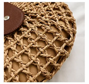 Detail view of khaki woven mesh, brown leather flap and silver metal buckle on straw bag