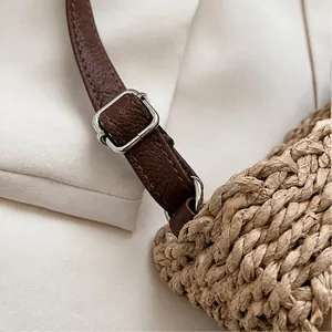 Detail of adjustable brown leather strap with silver buckle on woven straw bag