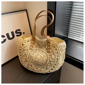 Detalle de bolso de paja con correas marrones reforzadas con costuras en X y forro interior