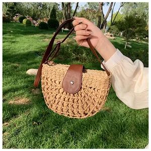 Detail of straw woven half-moon bag with hollow patterns and brown leather strap