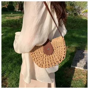 Detail of handmade straw half-moon bag featuring brown leather strap and magnetic clasp