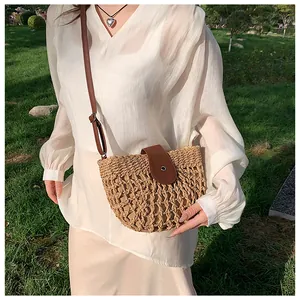 Detail of straw woven crossbody bag with brown leather flap and metallic buckle on grass