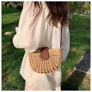 Detail of a semi-circular straw woven crossbody bag with brown leather strap and metal clasp