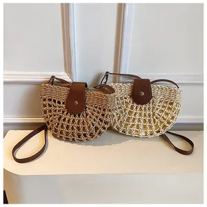 Detail of hollow woven straw bags in beige and khaki with brown leather flaps and strap