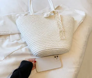 Detail of woven straw beach bag with lace ties and size reference next to a phone