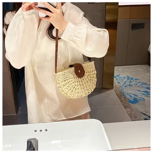 Close-up of semi-circle straw woven bag with brown leather flap and silver buckle