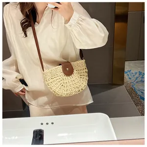 Detail of a semi-circular straw crossbody bag with brown leather strap and metal button