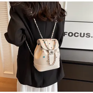 Close-up of cream mini backpack with colorful studs and silver chain shoulder straps