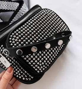 Détail d'un sac en cuir noir avec des clous argentés et une bandoulière géométrique