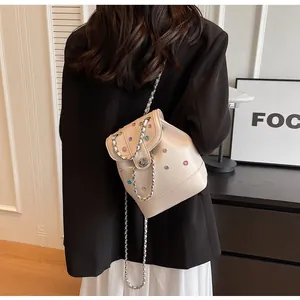 Detail view of a cream mini backpack with rhinestones and metal chain strap on model