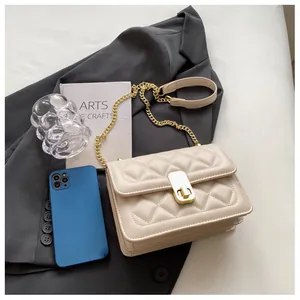 Détail du sac beige matelassé à chaîne avec fermoir doré posé sur une veste grise