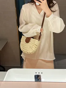 Beige straw woven saddle bag with brown leather strap worn by a woman for vacation style
