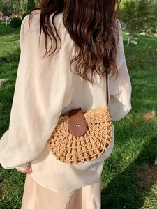 Woven straw crossbody bag with leather flap and semi-circular hollow design on green grass