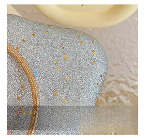 Macro detail of silver glitter fabric with star accents and gold chain on evening bag