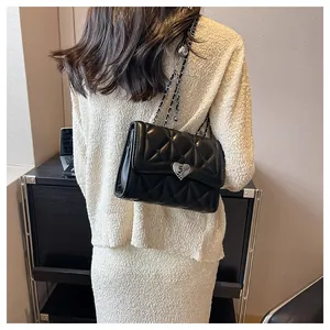 Détail du sac matelassé noir avec boucle cœur argentée porté à l'épaule par un mannequin