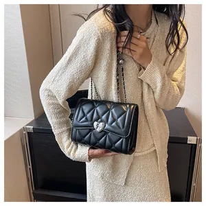 Détail du sac bandoulière matelassé noir avec boucle cœur argentée sur modèle élégant